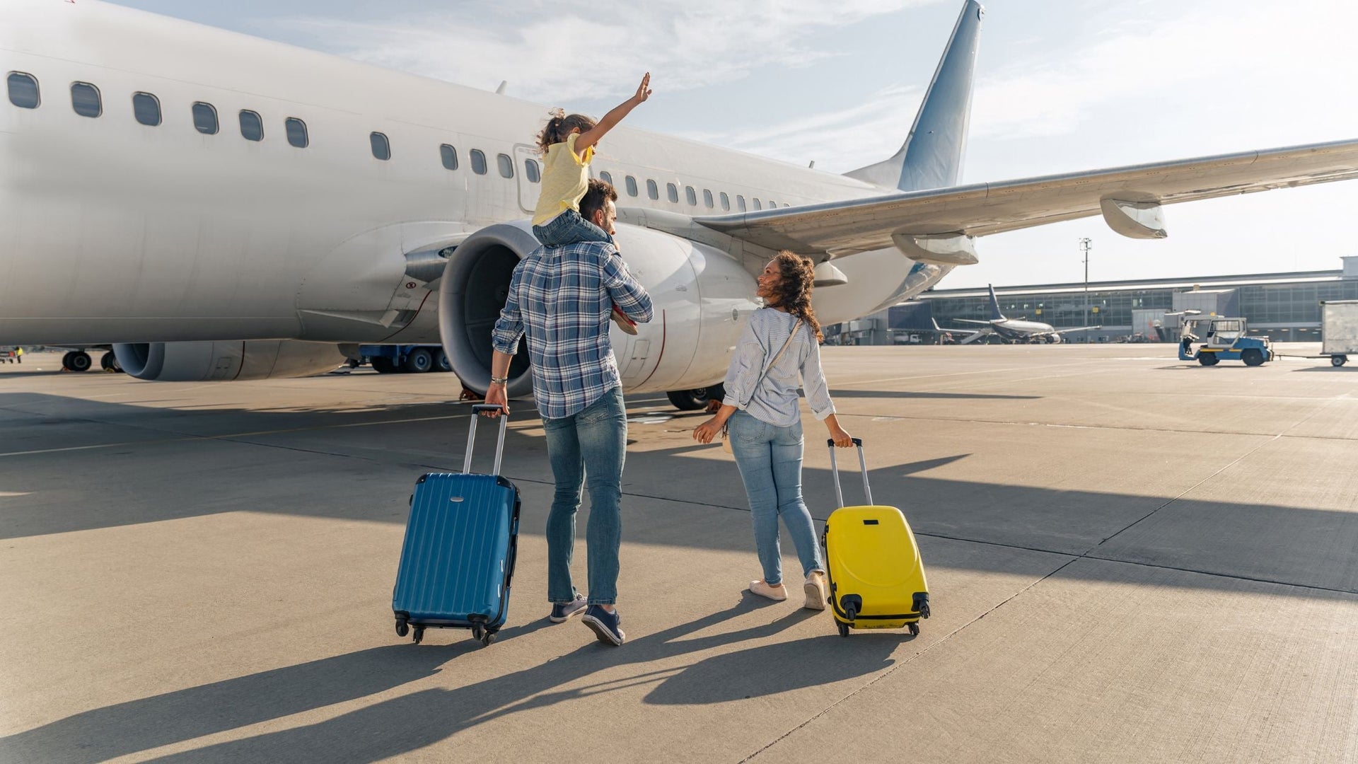 Family arriving at airport with luggage, preparing to board a plane on the tarmac.