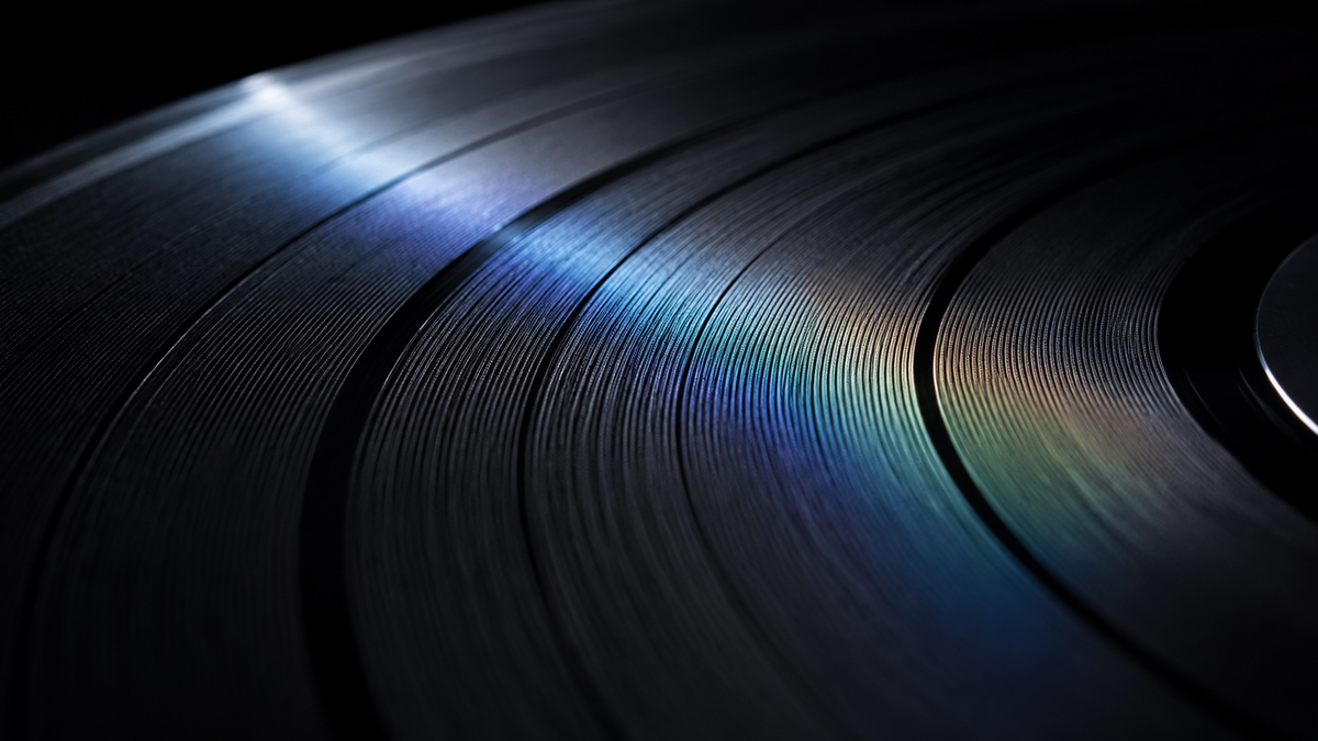Close-up of black vinyl record grooves reflecting subtle blue and amber light.